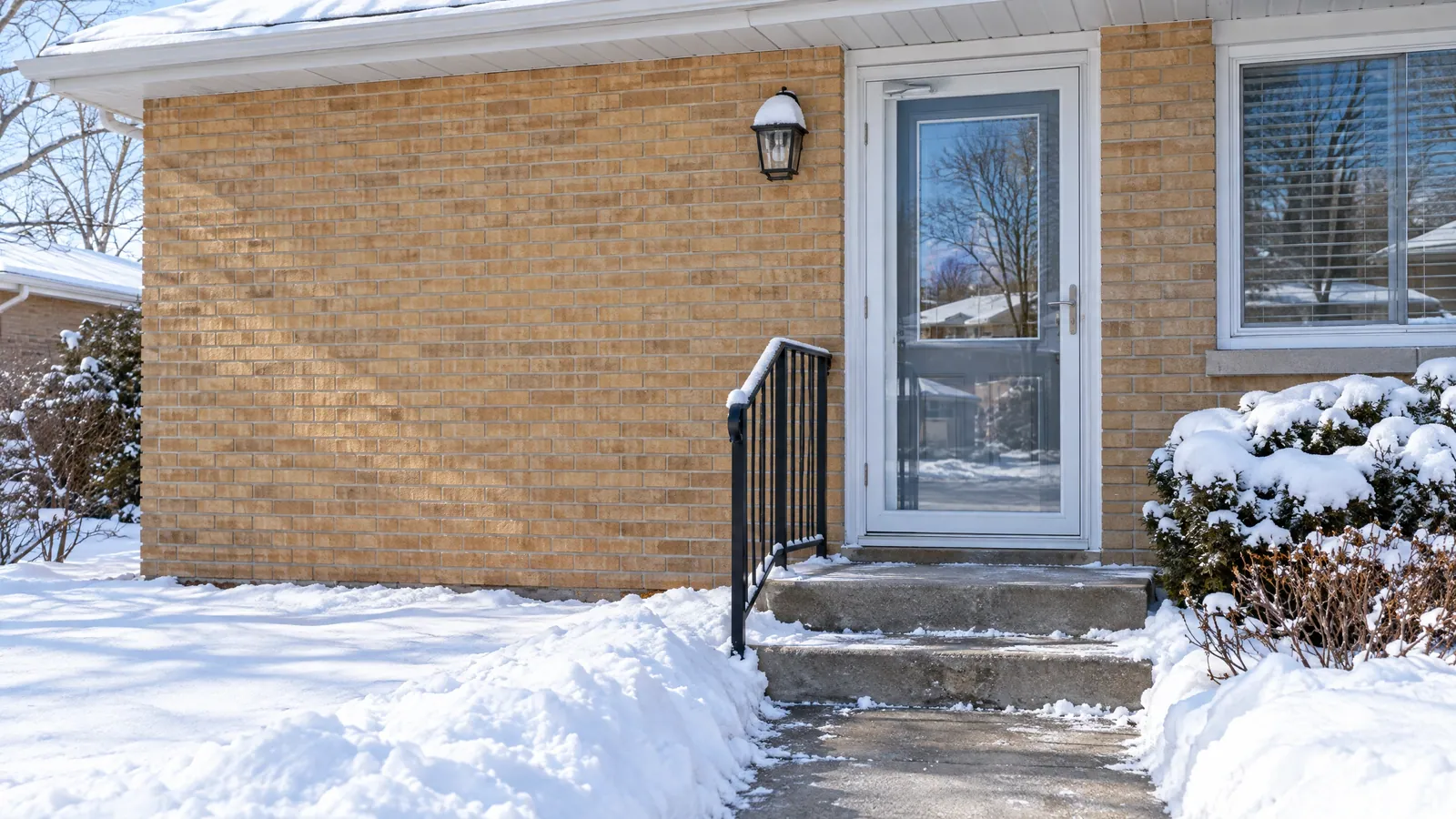 Fibreglass front door with a half-glass lite behind an aluminum storm door on a snowy 1950s brick bungalow