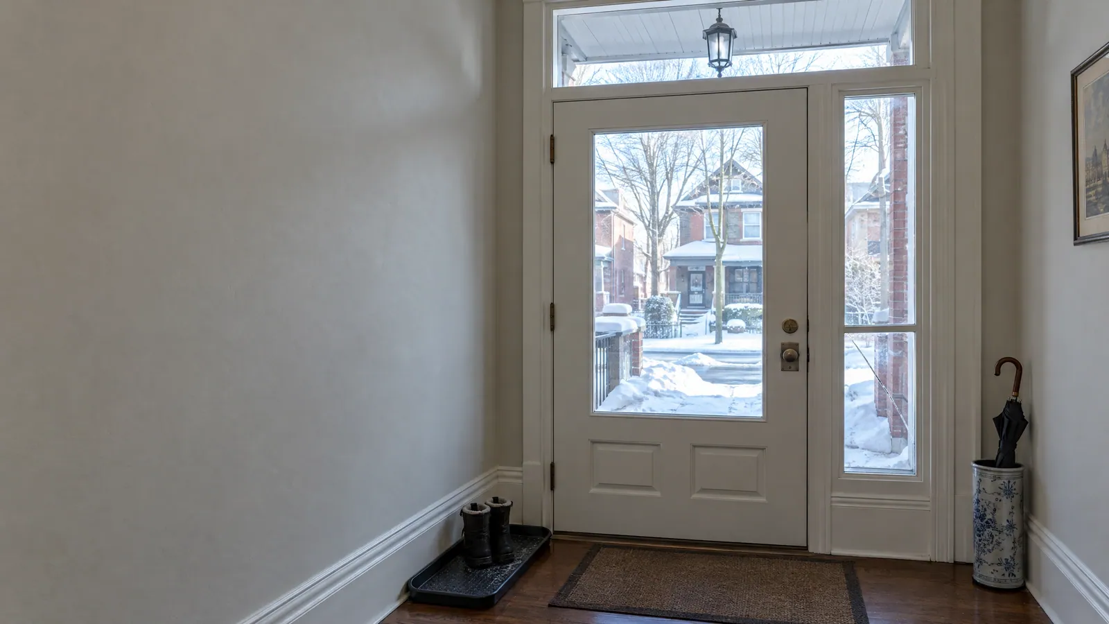 Vestibule of an older brick house: a glass front door, a cracked sidelight and a transom, with snow on the porch outside
