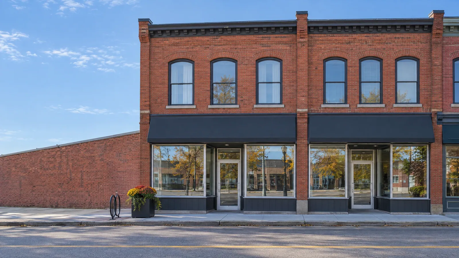 Two-storey red-brick main-street block with dark awnings over aluminum-framed shop windows and arched apartment windows above