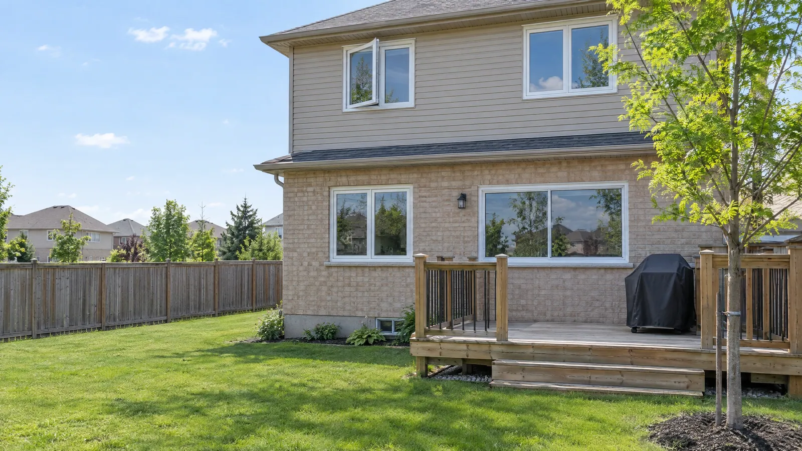 Back of a 1990s brick and siding house with white vinyl casement windows and a vinyl slider above a wood deck